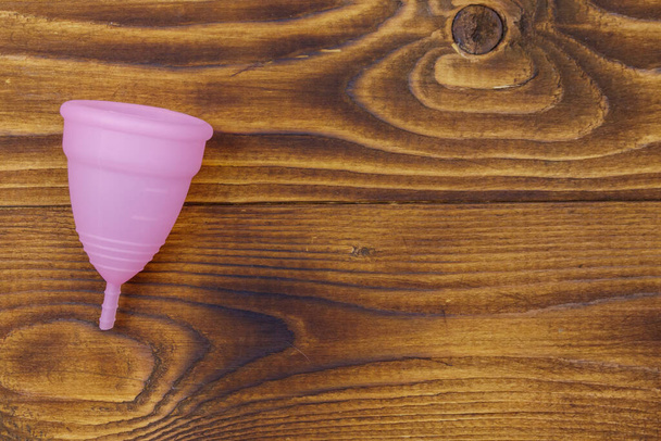 Růžové opakovaně použitelný silikonový menstruační šálek na dřevěném pozadí. Horní pohled, kopírovací prostor. Koncepce ženské hygieny, gynekologie a zdraví - Fotografie, Obrázek