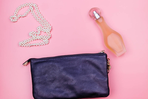 Сумка для сцепления, жемчужное ожерелье и бутылка духов на розовом фоне. Вид сверху. Концепция красоты и моды
 - Фото, изображение