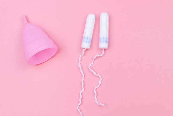 Różowy silikonowy kubek menstruacyjny wielokrotnego użytku i tampony na różowym tle. Widok góry. Pojęcie higieny kobiecej, ginekologii i zdrowia - Zdjęcie, obraz
