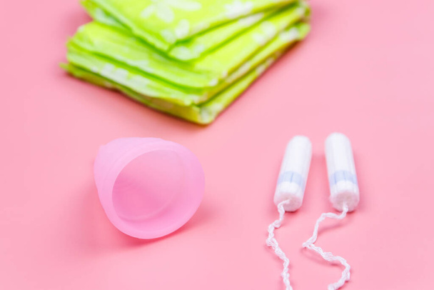 Санитарная прокладка, тампоны и менструальная чашка на розовом фоне. Концепция критических дней, менструации, женской гигиены - Фото, изображение
