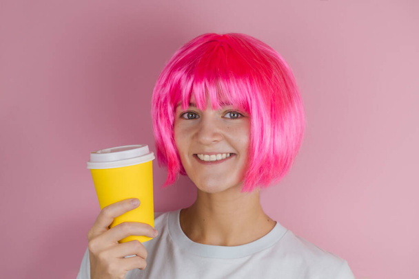 pretty happy young woman holding yellow  coffee to go cup against pink background - 写真・画像