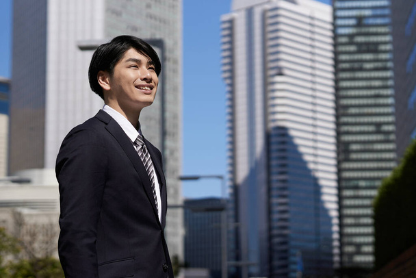 Hymyilevä japanilainen liikemies seisoo toimistoalueella
. - Valokuva, kuva