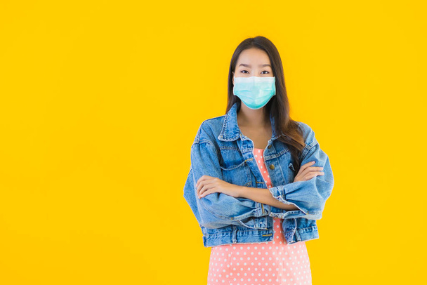 Портрет красивая молодая азиатская женщина носить маску для защиты коронавируса или covid19 на желтом изолированном фоне
 - Фото, изображение