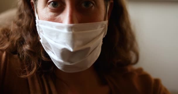 Portrét bělošky, která tráví čas doma, izoluje se a společensky se distancuje v karanténě během epidemie koronaviru covid 19, nosí masku a dívá se do kamery - Záběry, video