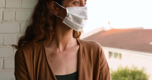 Caucasian woman spending time at home self isolating and social distancing in quarantine lockdown during coronavirus covid 19 epidemic, wearing a face mask and looking away - Filmati, video