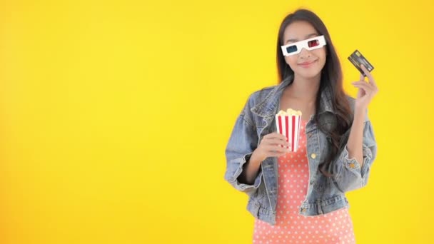 footage of beautiful Asian woman with popcorn and 3d goggles isolated on yellow - Felvétel, videó