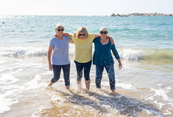 Lovely group of three senior retired woman on their 60s walking and having fun on the beach. Mature females Laughing and kicking water smiling playful enjoying retirement lifestyle and friendship. - Fotoğraf, Görsel