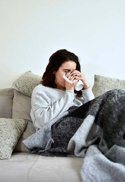 Молода дівчина п'є чай на сірому дивані
 - Фото, зображення