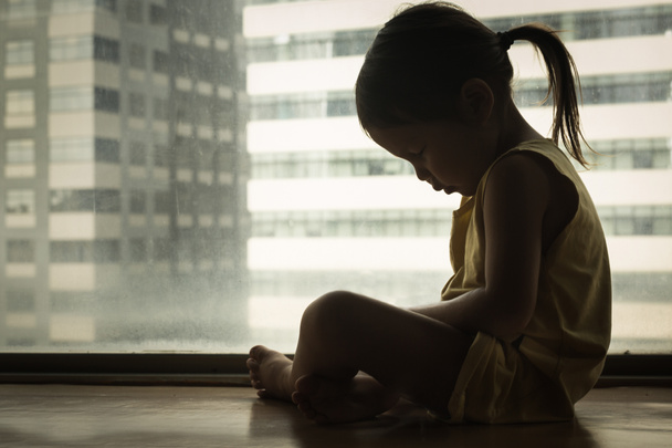 Mała dziewczynka siedząca obok okna z opuszczoną głową w smutku. uczucie depresji i bólu. - Zdjęcie, obraz