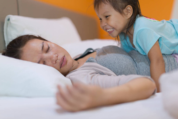 eine müde Mutter versucht, sich auszuruhen, während ihr Kind sie beim Versuch, sie aufzuwecken, stört. - Foto, Bild