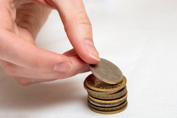 Saving money, a hand puts coins of different countries in a pile, white background, close-up. - Photo, Image
