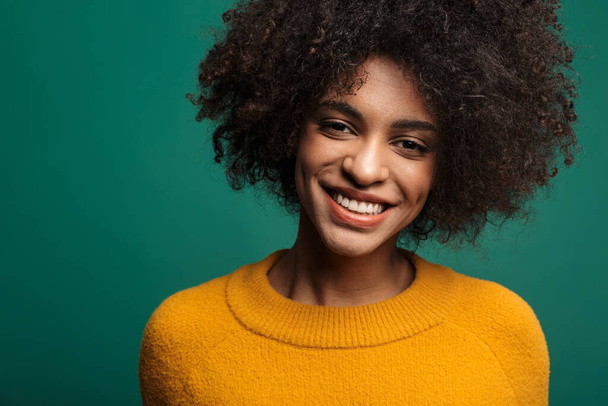 Portrait of a smiling young african woman wearing sweater standing isolated over green background, looking at camera - Fotografie, Obrázek