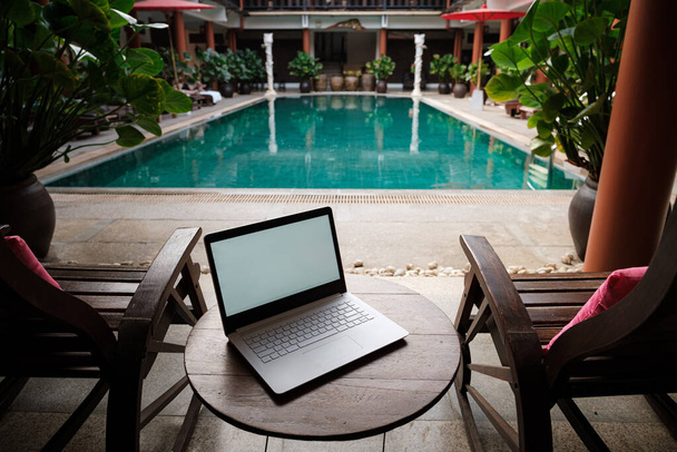 A white laptop on wooden table swiming pool background. A start of new day. Freelance business concept. Flexible remote working, travelling, advert and copy space - Photo, Image