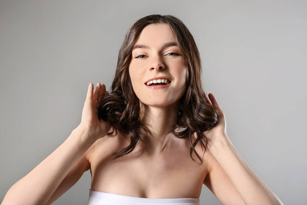 Νεαρή γυναίκα με όμορφα κοντά κυματιστά μαλλιά σε γκρι φόντο - Φωτογραφία, εικόνα