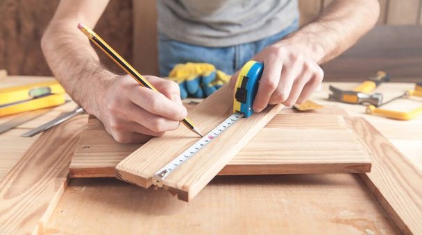 Плотник измеряет деревянную доску и делает отметки карандашом
. - Фото, изображение
