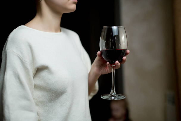 Girl holds a glass with red wine, standing near the curtained window. Close up, no face - Фото, зображення