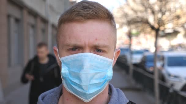 Πορτρέτο του νεαρού άνδρα με ιατρική μάσκα προσώπου στέκεται στο δρόμο της πόλης. Ένας τύπος που φοράει προστατευτική μάσκα από τον έξω κόσμο του ιού. Έννοια της ζωής για την υγεία και την ασφάλεια από την πανδημία του coronavirus - Πλάνα, βίντεο