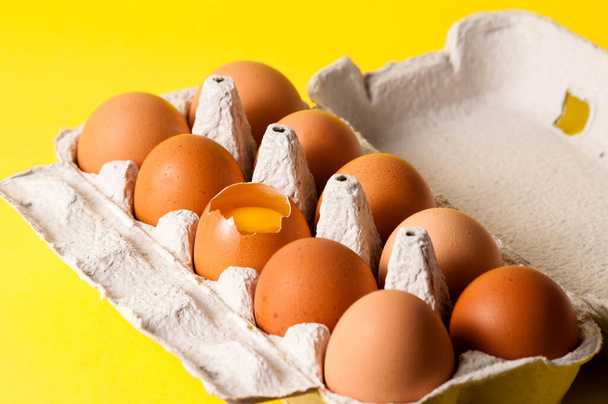 Large chicken eggs in a tray on yellow background, visible yolk - Photo, Image