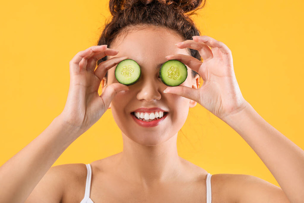 Beautiful young African-American woman with cucumber slices on color background - Foto, Bild