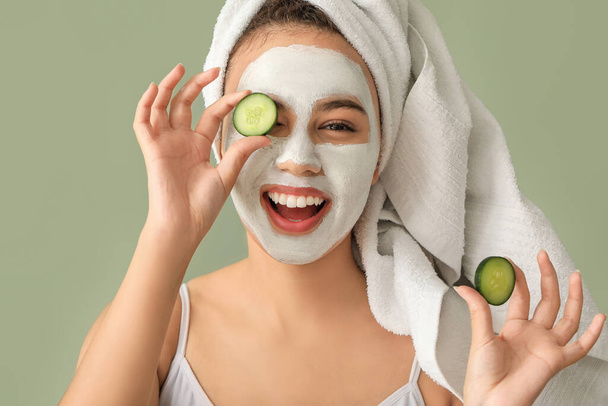 Beautiful young African-American woman with cucumber slices and facial mask on color background - Photo, Image