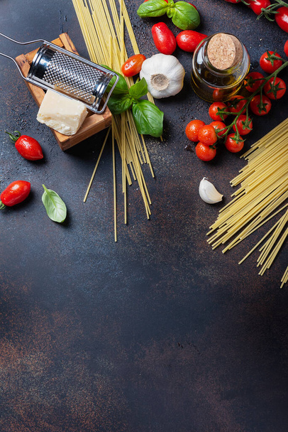Concept of italian food: spaghetti, tomato, basil, garlic, cheese and olive oil on the black table. Top view with a copy space - Photo, Image