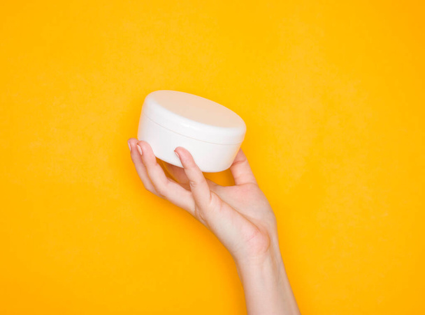 Une main de femme avec un pot de crème en plastique blanc. Produits cosmétiques de soins
. - Photo, image