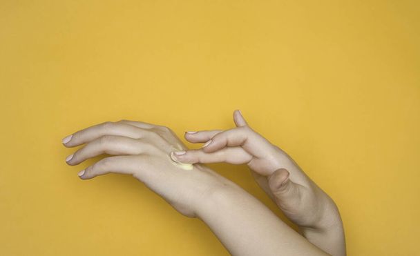 One hand smears the other hand with cream. Moisturizing cream, skin care cosmetics. Yellow background. - Photo, Image
