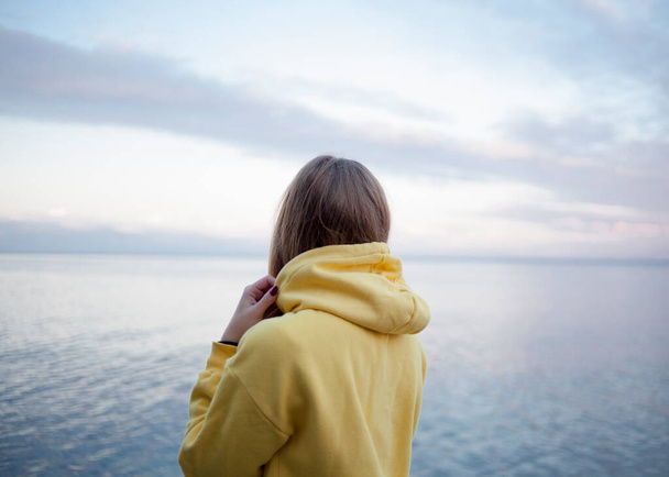 Tyttö keltaisessa paidassa seisoo rannalla ja katsoo merta.
 - Valokuva, kuva