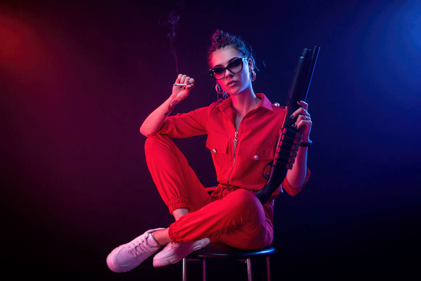 bruna brillante in una tuta rossa con un fucile su uno sfondo scuro in luce al neon
 - Foto, immagini