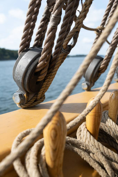 A vertical closeup shot of the ropes, the cable and the pulleys on a wooden sailing boat on the sea - Fotoğraf, Görsel