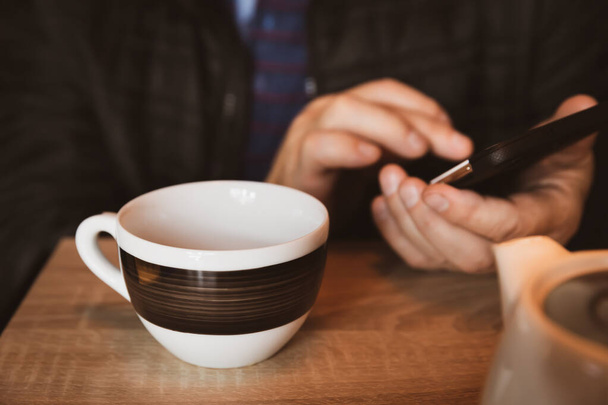 Egy férfi pihen egy kávézóban, teát iszik, üzeneteket olvas és ír egy okostelefonon. Dolgozz a mobil irodában. Egész napos kommunikáció. Közelkép lágy fókusz kép sekély mélységű mezővel - Fotó, kép