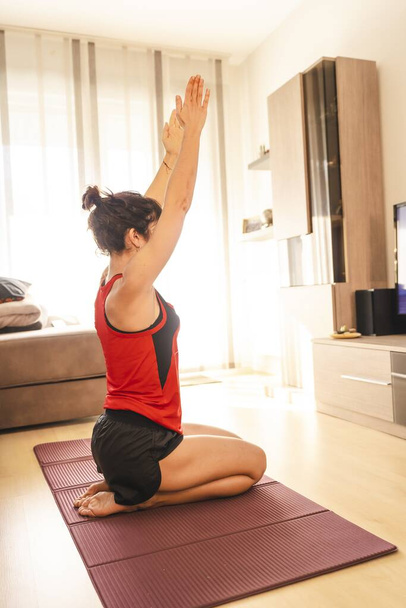 PASAIA, SPAIN - Apr 18, 2020: A young brunette doing exercises at home in the covid19 quarantine, raising her arms while watching TV - Foto, Imagem