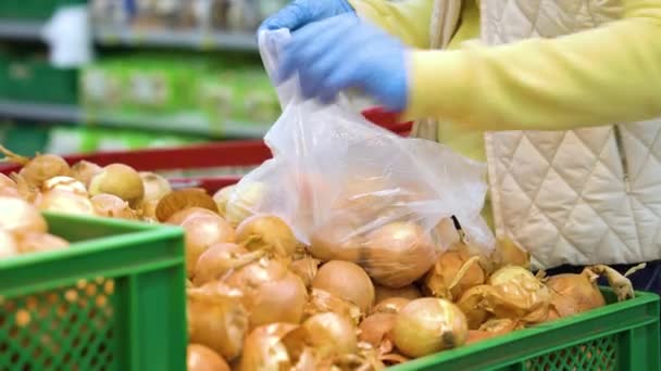 Crop woman in medical gloves putting onions in plastic bag at grocery store - Záběry, video