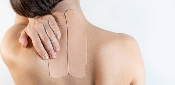Kinesiology beige taping on the human back on a gray background with a copy space. Dynamic functional bandage taping on the girl's neck. Solution for back and neck pain. Headache.  - Photo, Image