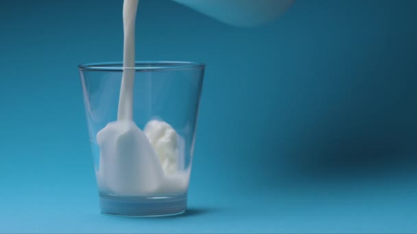 Milk is poured into a milk glass on a blue background. - Filmati, video