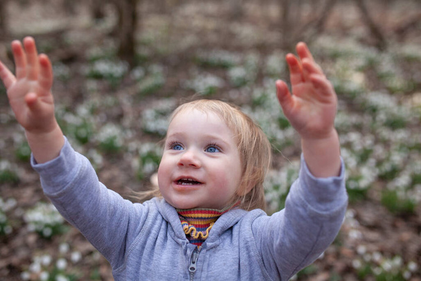 Kleines hübsches Mädchen auf einer Lichtung von Schneeglöckchen. Ein Kind spaziert im Frühlingswald. - Foto, Bild
