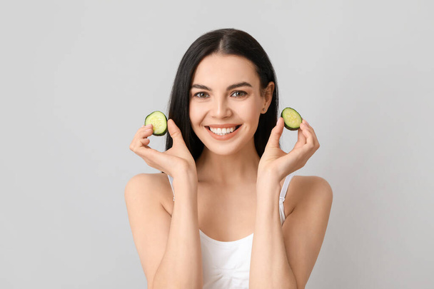 Beautiful young woman with cucumber slices on light background - Fotografie, Obrázek