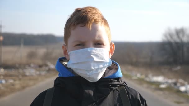 Πορτρέτο του μικρού αγοριού με ιατρική μάσκα προσώπου στέκεται σε εξωτερικούς χώρους. Θλιμμένο αρσενικό παιδί που φοράει προστατευτική μάσκα από τον ιό έξω. Έννοια της ζωής για την υγεία και την ασφάλεια από το coronavirus και πανδημία. Κλείσε. - Πλάνα, βίντεο