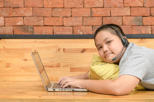 Elhízott fiú diák viselni fejhallgató tanulmány online tanár otthon, Boldog fiú diák játszik számítógép headset és élvezze az online tanulás nyaralás otthon. Kovid-19 - Fotó, kép