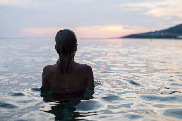Girl in the water watching sunset. Wet hair. Back view. - Photo, Image