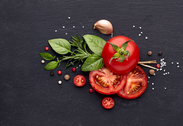 Verse basilicumbladeren met tomaten, peper, rozemarijn en knoflook op zwarte stenen ondergrond. Bovenaanzicht. - Foto, afbeelding