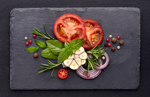 Fresh basil leaves with tomatoes, rosemary and garlic on black stone background. Top view. - Foto, imagen