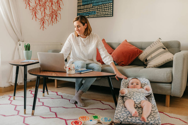 young business mother works from home with her laptop, with her baby by her side having fun - Φωτογραφία, εικόνα