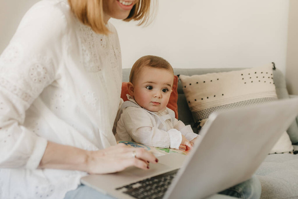 молодая деловая мать работает из дома со своим ноутбуком, с ребенком рядом с ней весело
 - Фото, изображение