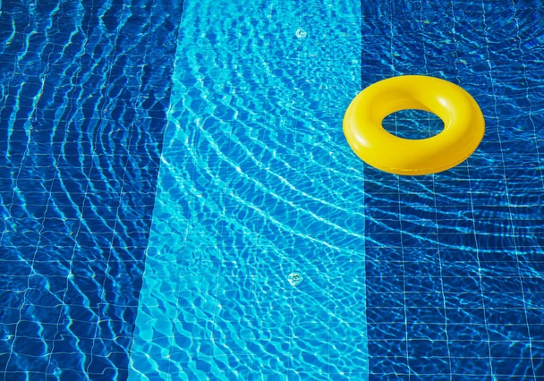 Flotador amarillo de la piscina, anillo flotando en una refrescante piscina azul - Foto, Imagen