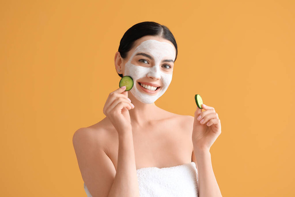 Beautiful young woman with cucumber slices and facial mask on color background - Foto, Imagen