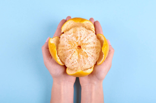 Hand with ripe and fresh orange fruit on blue background. Flat lay, overhead view image. - Fotoğraf, Görsel