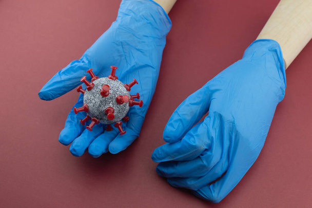 Manos de madera modelo con guantes azules y bola de retención similar a las células del coronavirus
. - Foto, Imagen