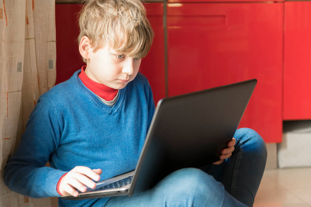 Блондинка дитина сидить на підлозі в кімнаті з ноутбуком. Домашнє господарство та освіта з дому онлайн, простір для тексту
 - Фото, зображення
