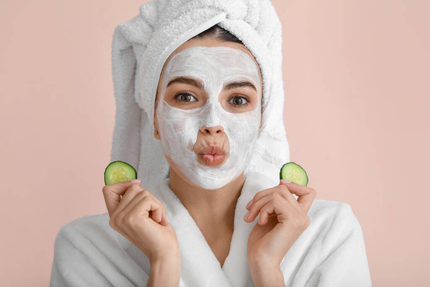 Beautiful young woman with cucumber slices and facial mask on color background - Foto, Imagem